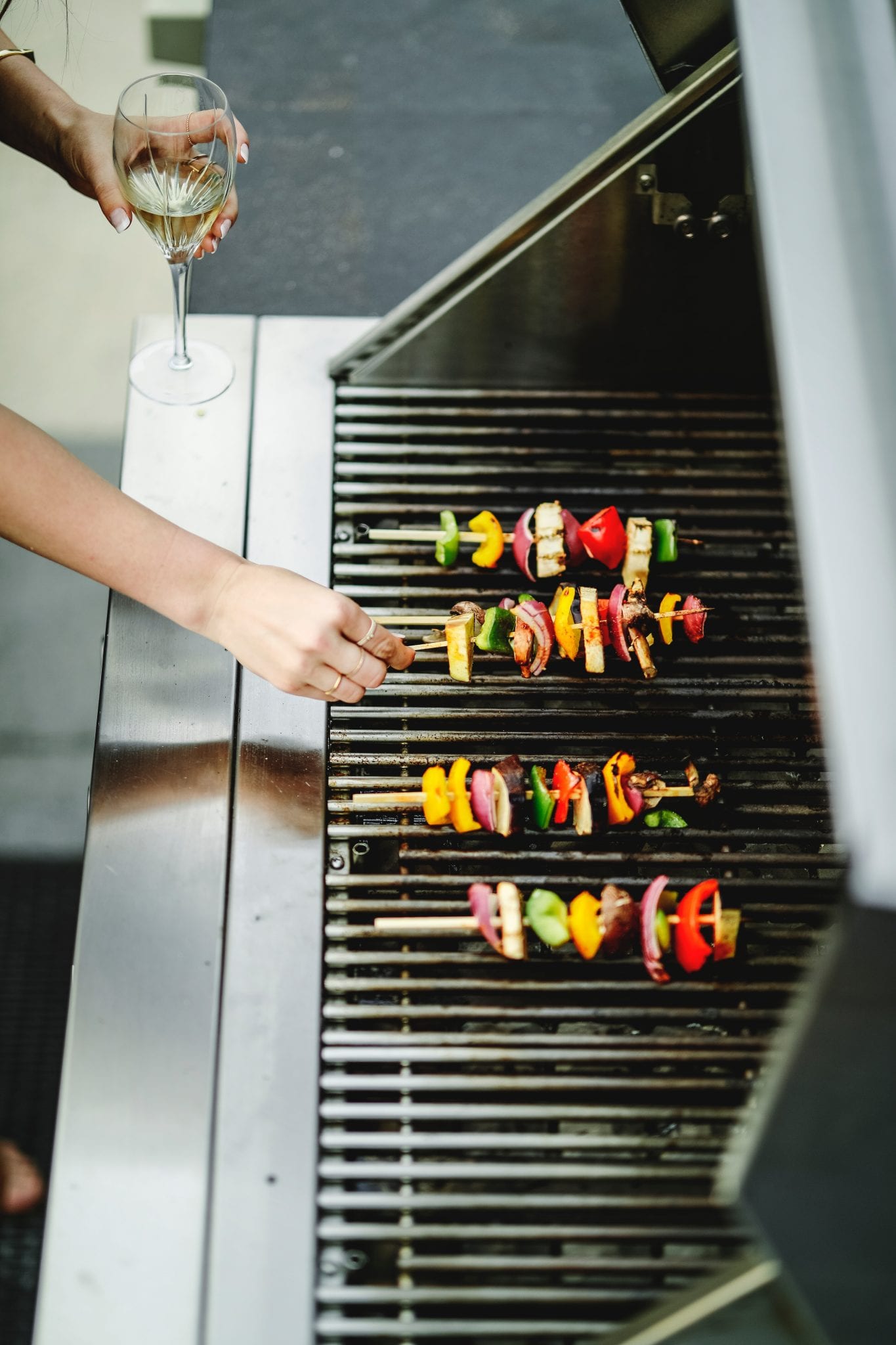 woman holding wine glass and flipping skewers on grill